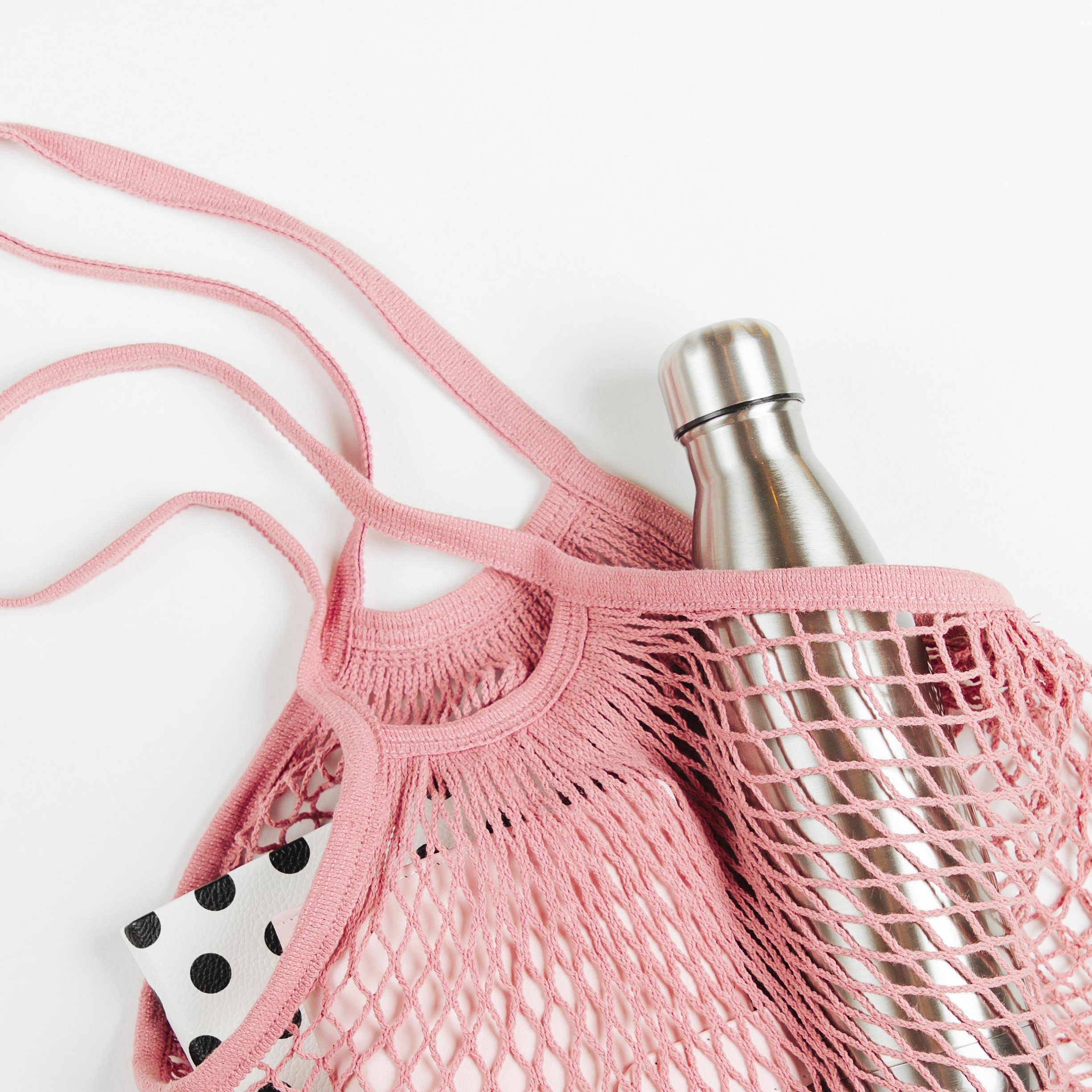 Stainless steel water bottle in pink mesh tote bag on white background, represents “Log Your Water Intake” program