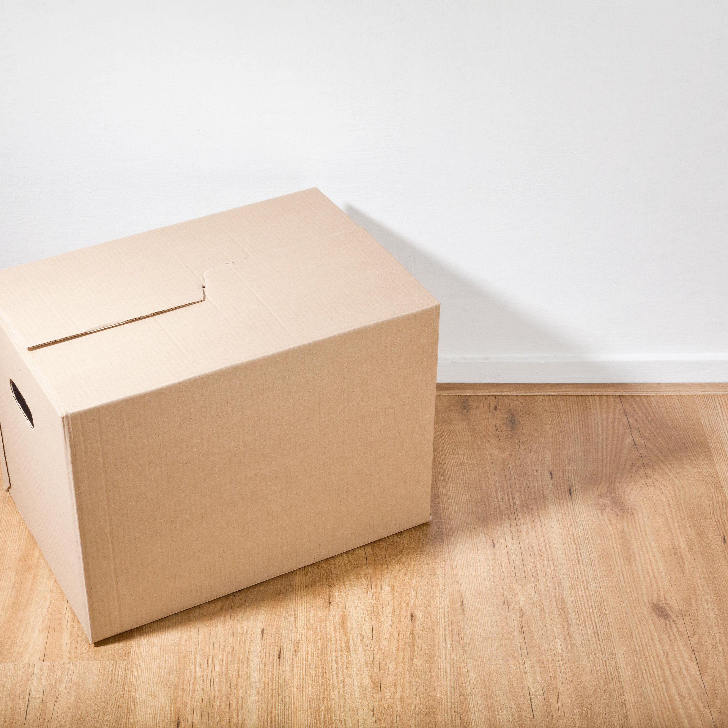 Moving box on wooden floor with white wall in background, represents “Match With a Roommate” program
